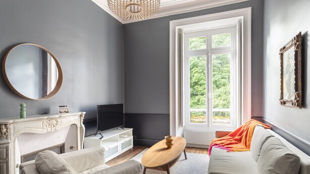A living room with a fireplace, television, sofa, and a large window with a view of greenery. - Modjesko - Au coeur de Rennes (Rennes)