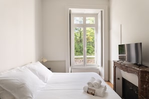 A hotel room with a bed, a television, and a window with a view of greenery.
