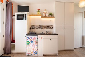 Une cuisine compacte équipée d’un four à micro-ondes, d’un évier et d’un réfrigérateur orné d’un motif floral coloré.