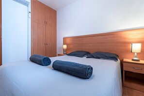 A neatly made bed with two rolled towels, a wooden headboard, a bedside lamp, and a wooden wardrobe. - L'Escapade Corse - À 80 mètres de la plage (San-Nicolao)