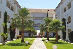 A courtyard with a central pathway, palm trees, and a building with multiple floors and balconies. - L'Escapade Corse - À 80 mètres de la plage (San-Nicolao)