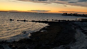 A coastal scene with a rocky shoreline, calm water, and a sunset sky.