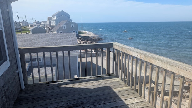 A wooden deck with a railing overlooking a rocky shoreline and a body of water.