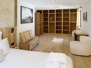 Ein Schlafzimmer mit einem Bett, einer Holzbank, einem weißen Stuhl, einem Holzschrank und einem gerahmten Bild an der Wand.