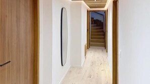 Un pasillo con suelo de madera, paredes blancas y techo de madera.