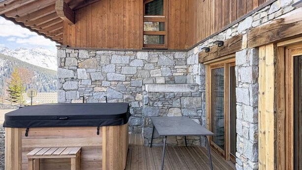 Eine Holzterrasse mit Whirlpool, einem kleinen Tisch und einer Steinmauer.