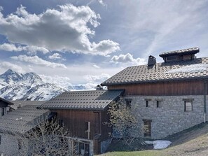 A traditional chalet with stone walls and wooden beams, set against a backdrop of snow-capped mountains and a partly cloudy sky. - 300m from ski slopes, view mountain, terrace, parking, ski locker, 117m², La Rosière (Montvalezan)