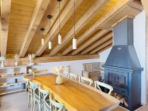 Eine rustikale Küche mit Holztisch, Stühlen, hängenden Pendelleuchten und einem Holzofen.