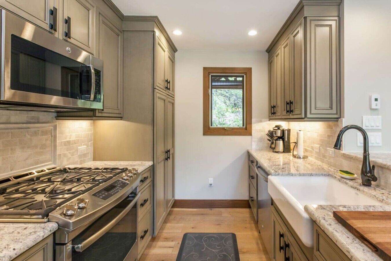 A kitchen with a gas stove, stainless steel microwave, and a window above the sink.