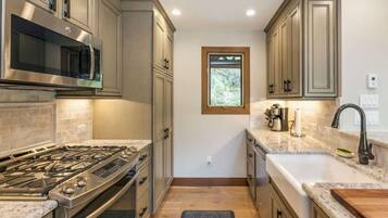 A kitchen with a gas stove, stainless steel microwave, and a window above the sink.