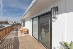 A deck with wooden flooring and two chairs, a sliding glass door, and a white exterior wall. - The SouthOhana Retreat (Oceanside)