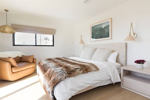 A bedroom with a bed, a sofa, a window with blinds, and a painting on the wall. - The SouthOhana Retreat (Oceanside)