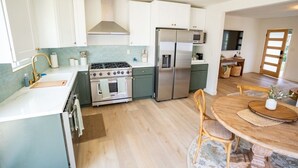Een moderne keuken met witte kastjes, roestvrijstalen apparatuur en een houten eettafel.