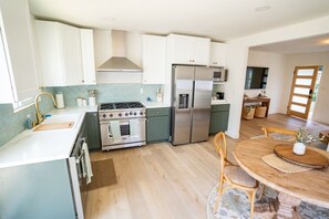 A modern kitchen with white cabinets, stainless steel appliances, and a wooden dining table. - BRAND NEW - Single-Family Solana Beach House, Steps from the Beach. (Solana Beach)