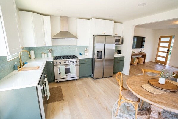 A modern kitchen with white cabinets, stainless steel appliances, and a wooden dining table.