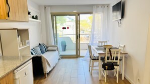 Una cocina moderna con lavavajillas integrado, una zona de comedor con mesa y sillas, un sofá y una puerta corrediza de vidrio que da a un espacio exterior con planta en maceta.