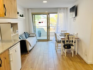 Eine moderne Küche mit integriertem Geschirrspüler, einem Essbereich mit Tisch und Stühlen, einer Couch und einer Glastür zum Außenbereich mit einem Blumentopf.