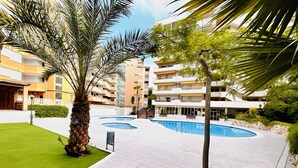 Un edificio residencial moderno con piscina, césped verde y palmeras.