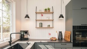 A modern kitchen with a built-in sink, a coffee maker, and a Siemens oven. There are wooden shelves with plants and kitchen items, and pendant lights above. - 4 Star Holiday Home in Ansager (Ansager)