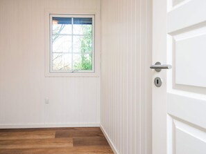 A room with a wooden floor, a window with a view of trees, and a white door with a silver handle. - 4 Star Holiday Home in Ansager (Ansager)
