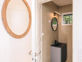 A bathroom with a wooden-framed mirror, a black sink, and a small window with a view of greenery.
