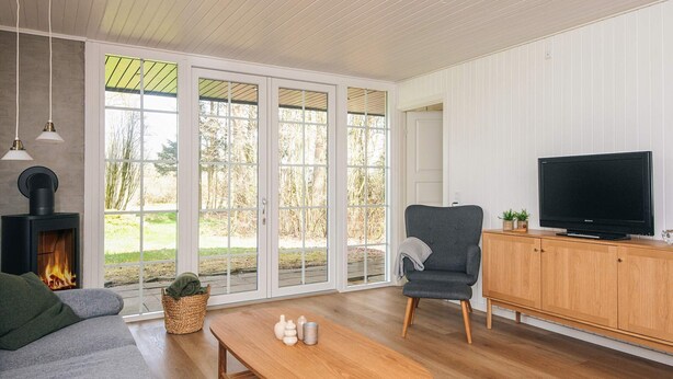 A modern living room with a fireplace, a sofa, a grey armchair, a wooden coffee table, and a television on a wooden cabinet. - 4 Star Holiday Home in Ansager (Ansager)