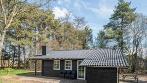 A small cabin with a tiled roof, a chimney, and a porch with two chairs. - 4 Star Holiday Home in Ansager (Ansager)