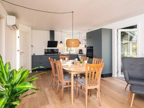 A modern kitchen with white cabinets, a black countertop, and a dining area with wooden chairs and a table. - 4 Star Holiday Home in Ansager (Ansager)