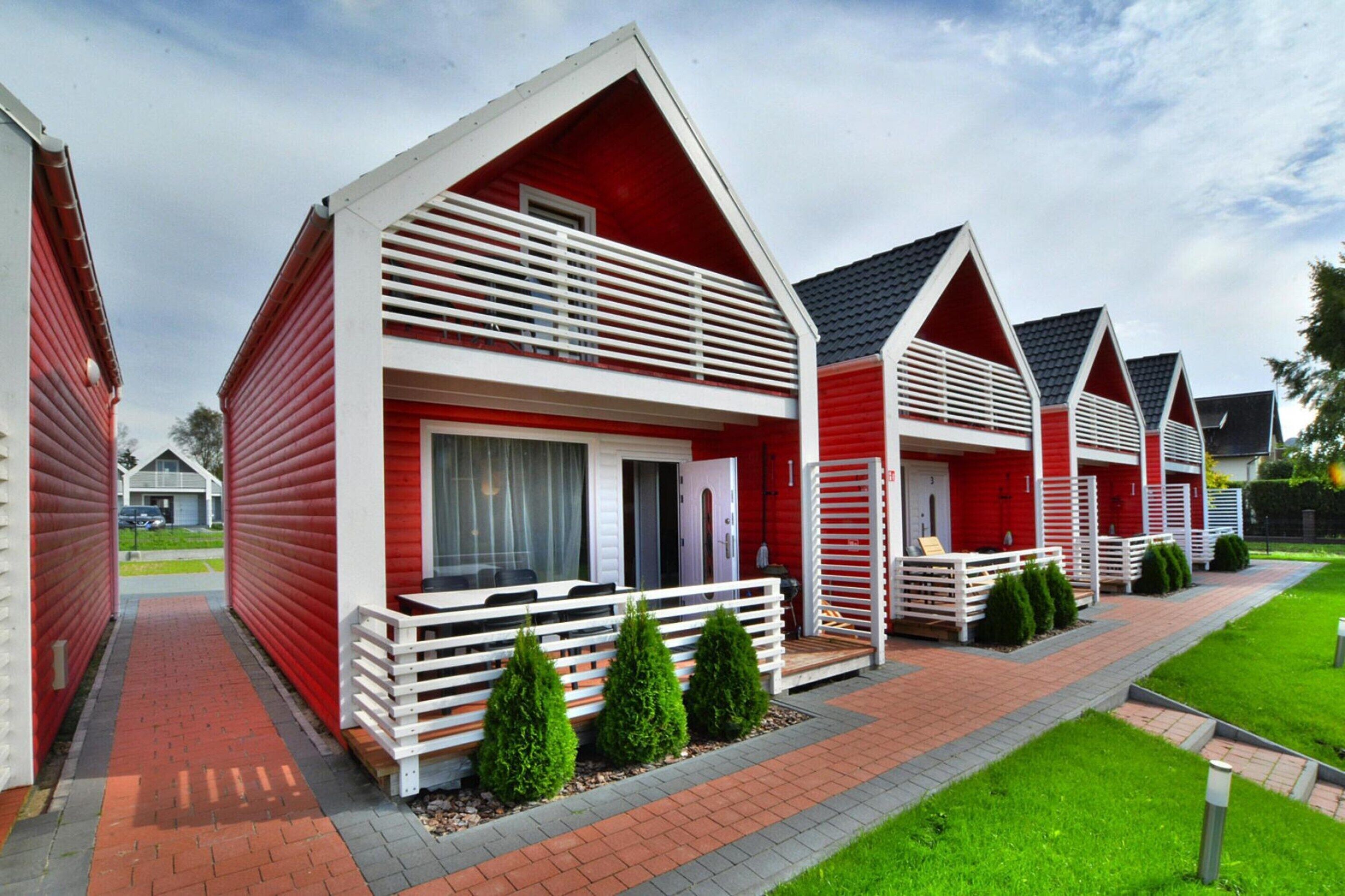 A row of red and white vacation cottages with balconies, a brick pathway, and green landscaping.