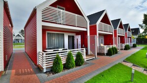 Une rangée de charmantes maisons de vacances aux couleurs rouge et blanche, dotées de balcons, un chemin bordé de briques et un aménagement paysager verdoyant.