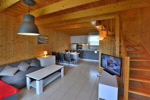 Ein Holzinnenraum mit Sofa, Esstisch, Fernseher, Küche und Treppe.