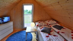 Une chambre mansardée chaleureuse avec un plafond en pente en bois, un téléviseur posé sur une commode, un lit avec une literie à motifs floraux rouges et une petite table avec une lampe.