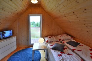 Ein gemütliches Schlafzimmer unter dem Dach mit Holzbalkendecke, einem Fernseher auf einer Kommode, einem Bett mit roten Blumenbettwäsche und einem kleinen Tisch mit Lampe.