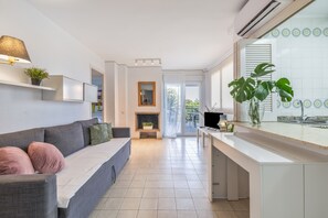 Una sala de estar moderna con un sofá gris, una chimenea, una zona de cocina con encimera blanca y un ventanal con vistas.