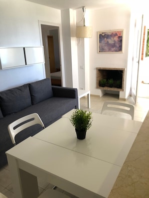 Un saló modern amb un sofà gris, una taula de dinar blanca i una petita planta en test.