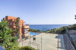 Un edificio residencial con piscina, cancha de tenis y vista al mar.