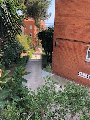 Un sender estret que condueix a un edifici amb façana de maó, envoltat de vegetació i un cel clar.