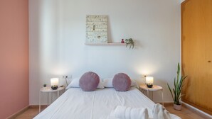 Una camera da letto ordinata con un letto, due comodini con lampade, uno scaffale a parete con una pianta e una porta in legno.