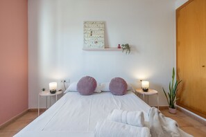 Et pænt møbleret soveværelse med en seng, to sengeborde med lamper, en vægmonteret hylde med en plante, og en trædør.