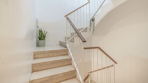 Eine Treppe mit Holzhandlauf und weißen Spindeln, ein Blumentopf auf der Zwischenebene und eine schlichte Wand.