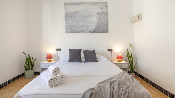 Ein Hotelzimmer mit einem Bett, zwei Nachttischen, einem Beistelltisch, einer Topfpflanze und einem an der Wand hängenden Kunstwerk.