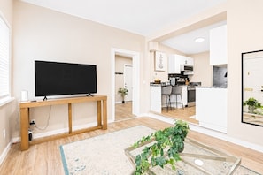 A living room with a TV, a wooden console table, a plant, and a kitchen in the background. - Walkerville 1BR Suite | Parking, Laundry & WiFi (Windsor)