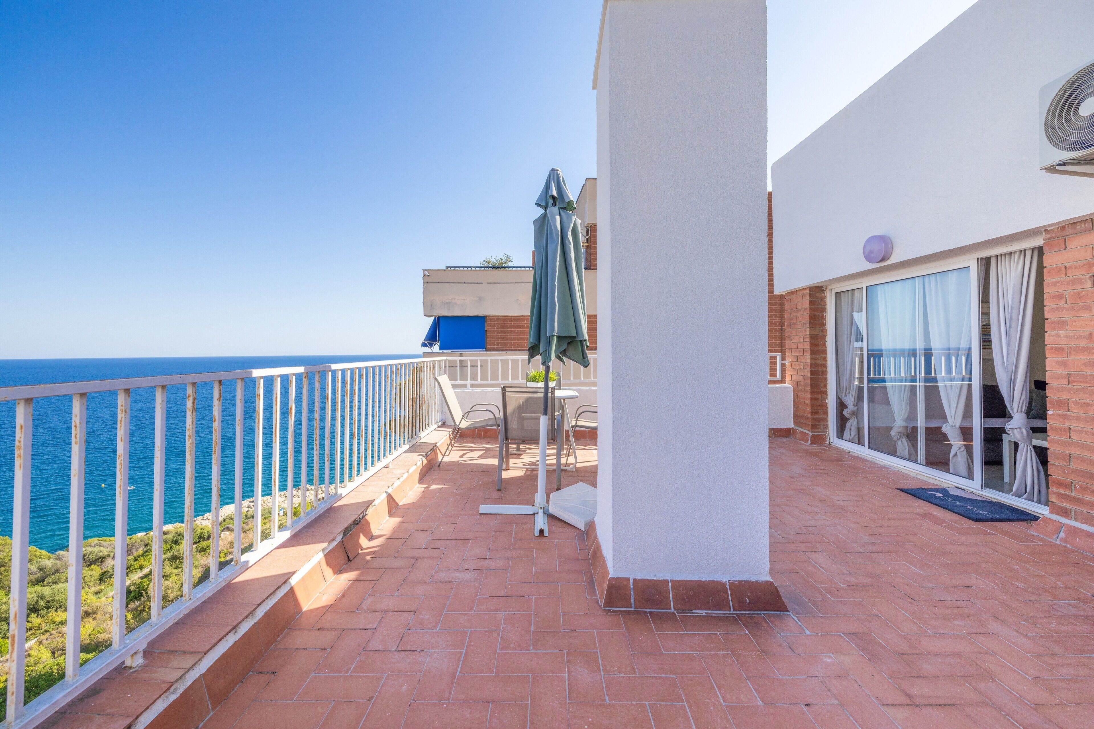 Een balkon met uitzicht op zee, een tafel met stoelen, en een overdekt terras met een tafel en stoelen.