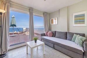 Une pièce avec un balcon, un canapé, une petite table et une plante en pot.