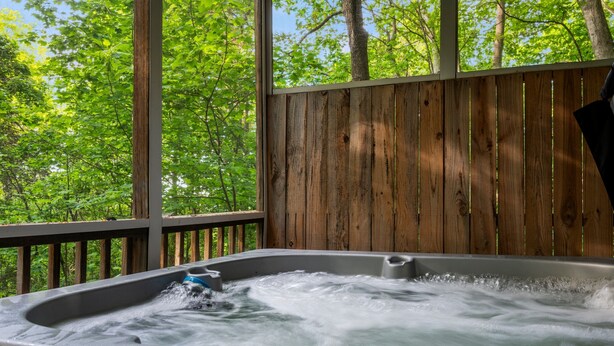 Een hottub met een houten terras en uitzicht op een bos.