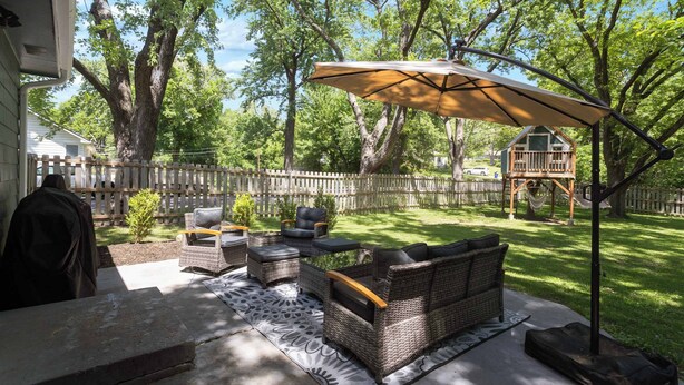 An outdoor patio with wicker furniture, a table, and a large umbrella. - Spacious 4BR Home_Fenced Yard_Patio_BBQ Grill (Overland Park)