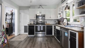 A modern kitchen with white cabinets, stainless steel appliances, and a wooden floor. - Spacious 4BR Home_Fenced Yard_Patio_BBQ Grill (Overland Park)
