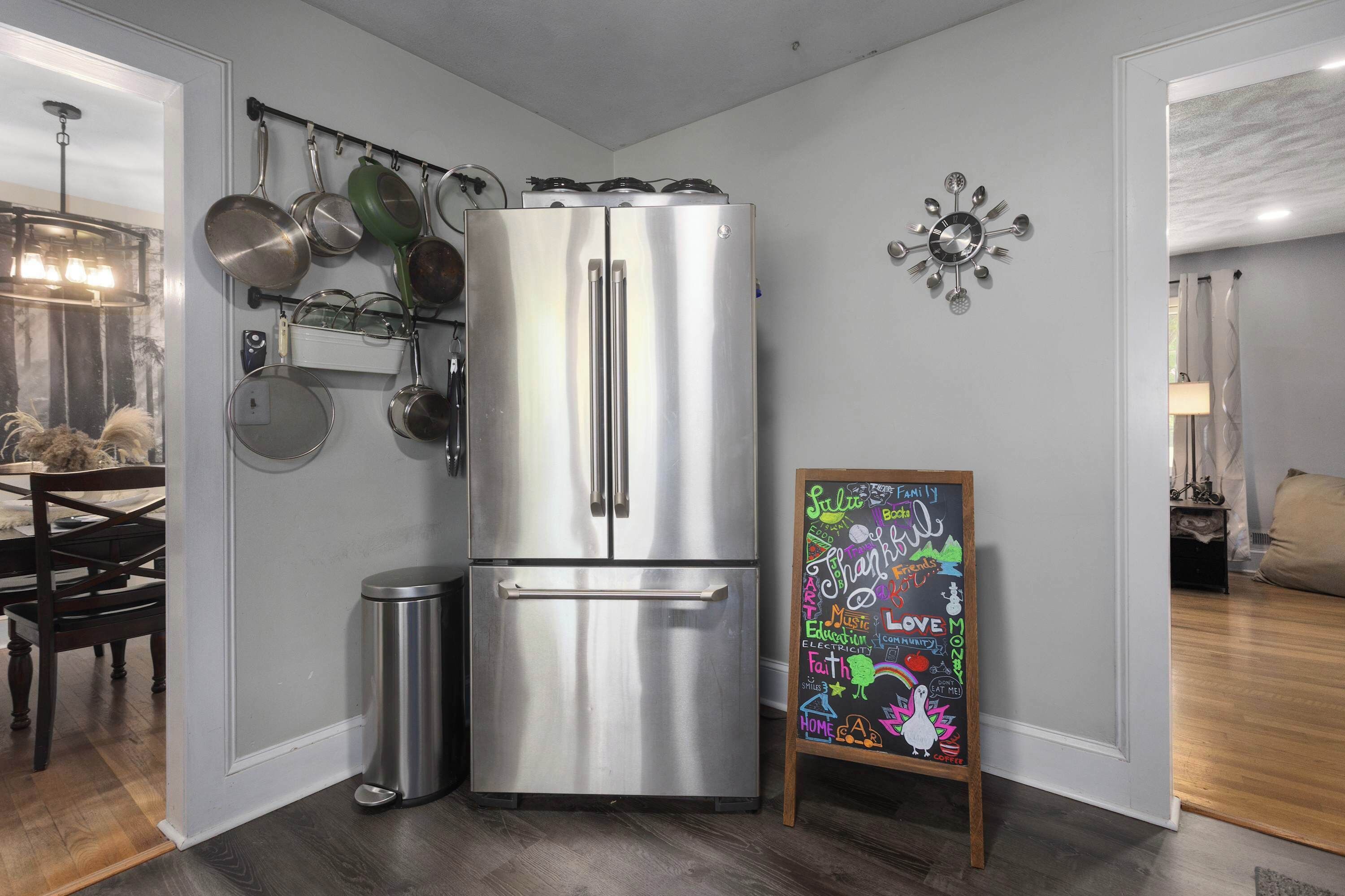 Une cuisine moderne avec un réfrigérateur en acier inoxydable, un tableau noir où sont écrits des mots liés à la famille, et une horloge murale décorative.