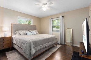 A bedroom with a bed, nightstand, lamp, ceiling fan, window, and a mirror.