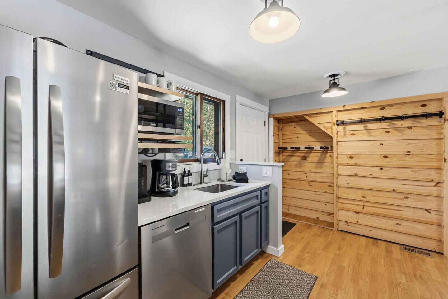A modern kitchen with stainless steel appliances, a coffee maker, and a wooden wall.